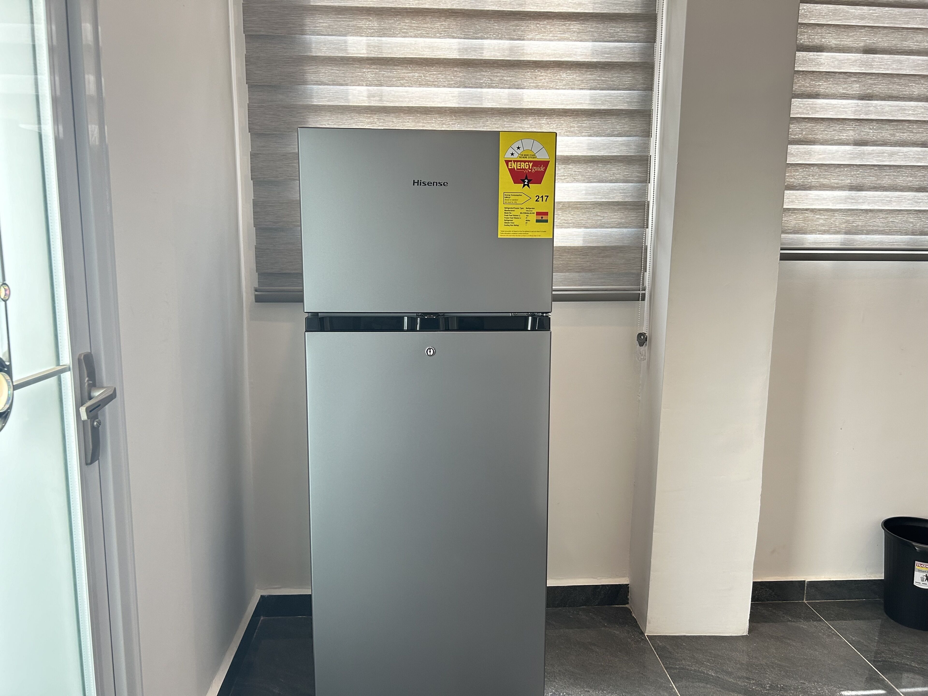 A Hisense refrigerator in a corner of a room with a window and a door.