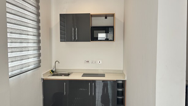 A compact kitchen with a built-in microwave, a sink, and a wooden countertop. - Mayama Residences  (Accra)
