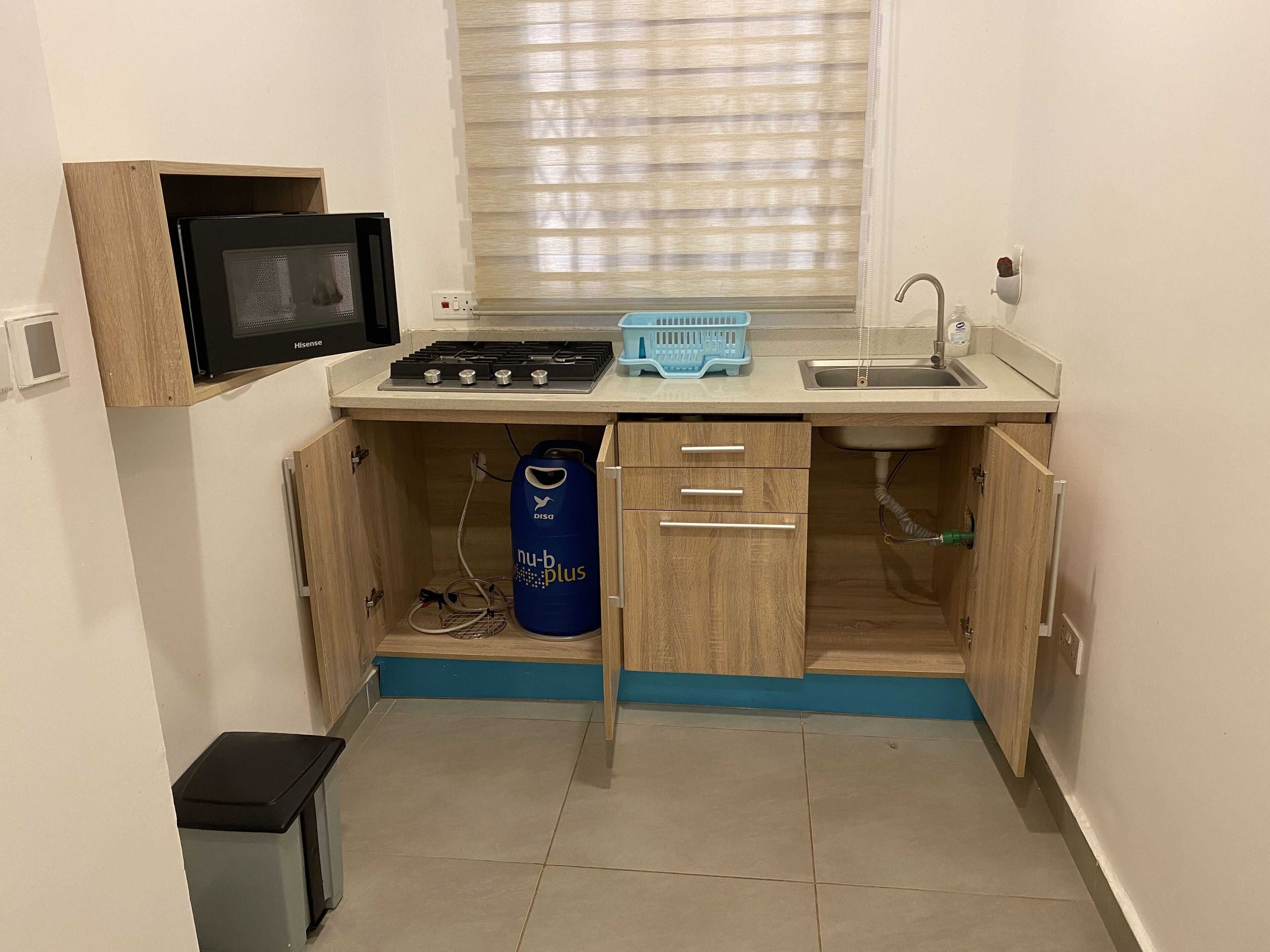 A compact kitchen with a microwave, stove, sink, and a blue water dispenser.