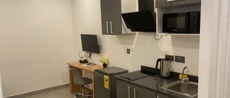Una kitchenette compacta con microondas, estufa y pileta. Hay un pequeño escritorio con una silla y una planta en maceta.