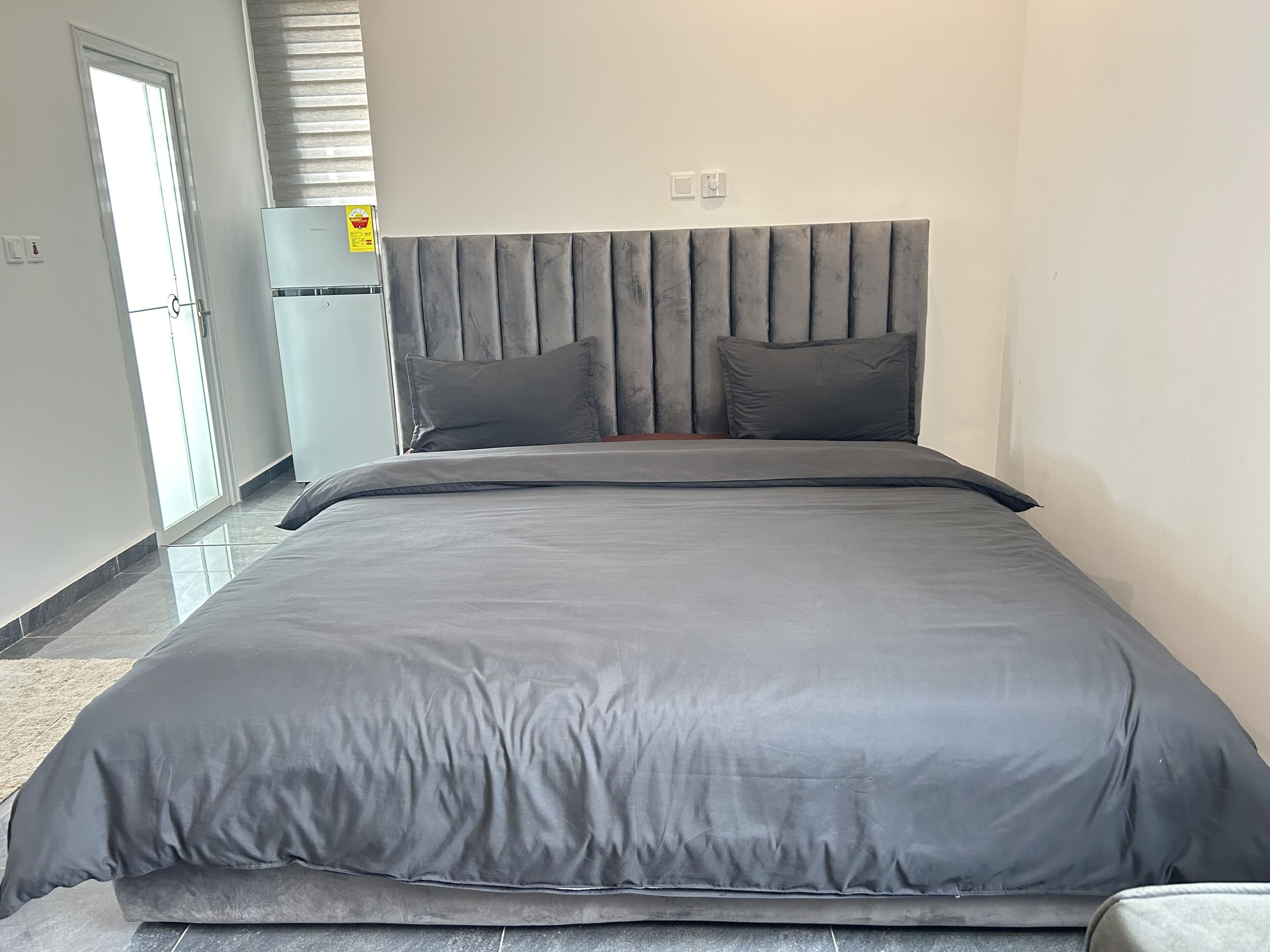 A modern bedroom with a large bed, grey bedding, and a headboard with vertical panels.