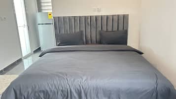 A modern bedroom with a large bed, grey bedding, and a headboard with vertical panels.