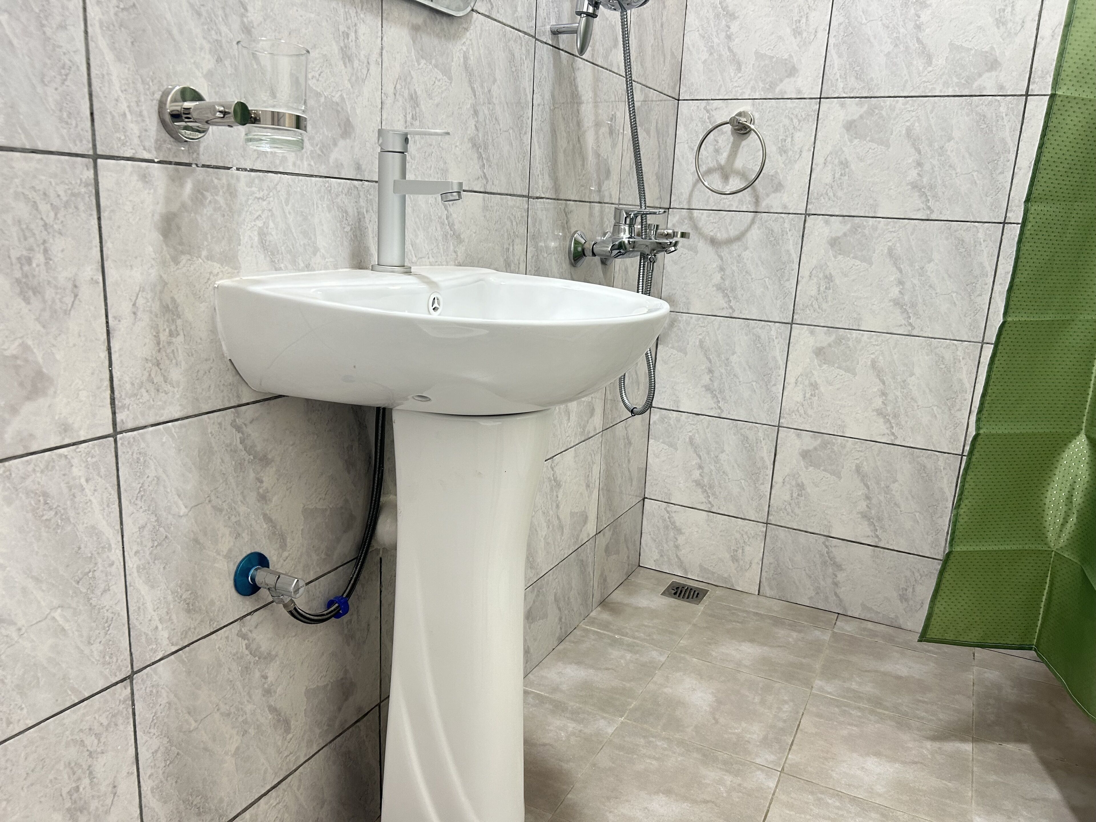A bathroom with a white pedestal sink, a handheld showerhead, and a green shower curtain.