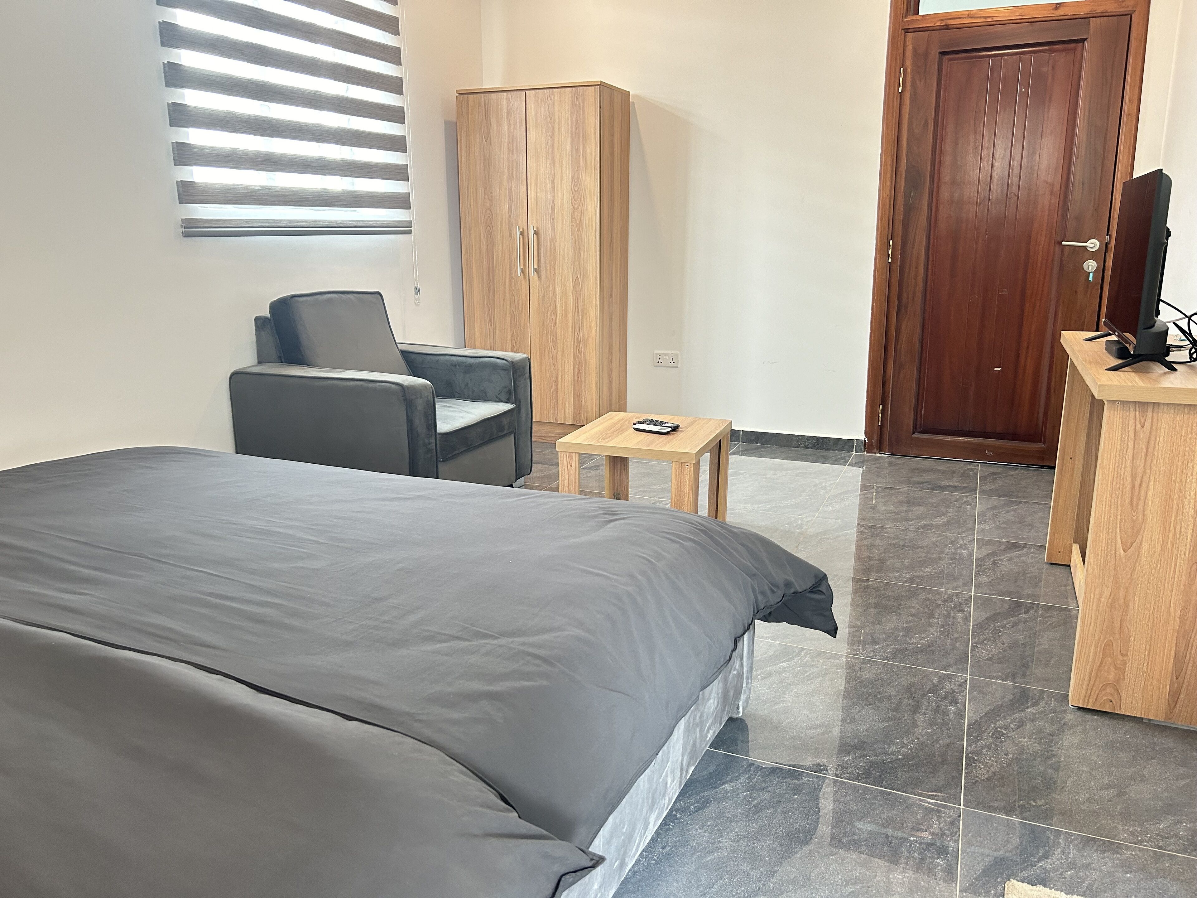 A bedroom with a bed, a chair, a wooden wardrobe, a small table, and a door.