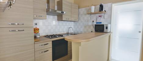 Una cocina moderna con gabinetes de madera clara, estufa integrada y microondas.