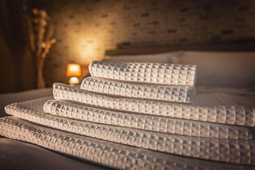 A stack of white, textured mattresses on a bed in a dimly lit room with a brick wall and a small lamp in the background.