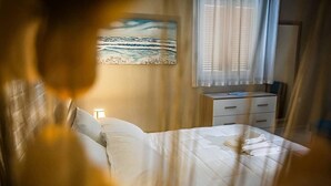 A bedroom with a bed, a nightstand, a drawer unit, and a painting of a beach scene. - Beachfront villa in Fiumicino, terrace & sunset (Isola Sacra)