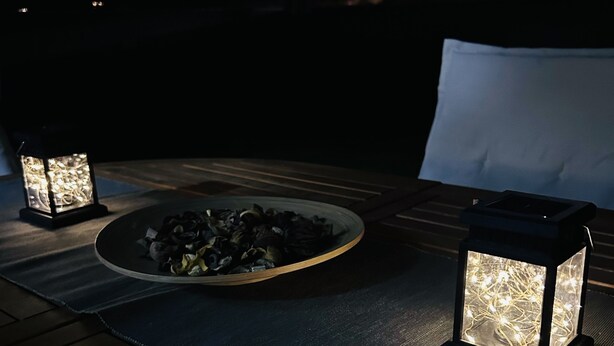A table set outdoors with a bowl of snacks and two illuminated lanterns.