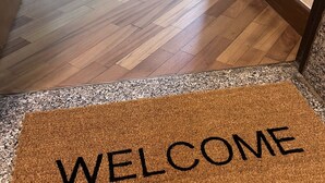A wooden floor leading to a room with a welcome mat.