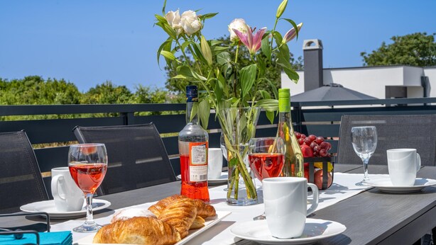 Una mesa dispuesta con croissants, copas de vino, una botella y un jarrón con flores.