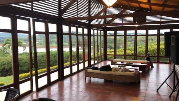 A spacious room with large windows offering a view of a lush landscape. There is a sofa and a dining table. - Casa Maria, Lagoon Calima (Club Las Anonimos)