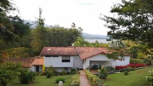 A white building with a red-tiled roof, surrounded by lush greenery and a pathway leading to the entrance. - Casa Maria, Lagoon Calima (Club Las Anonimos)