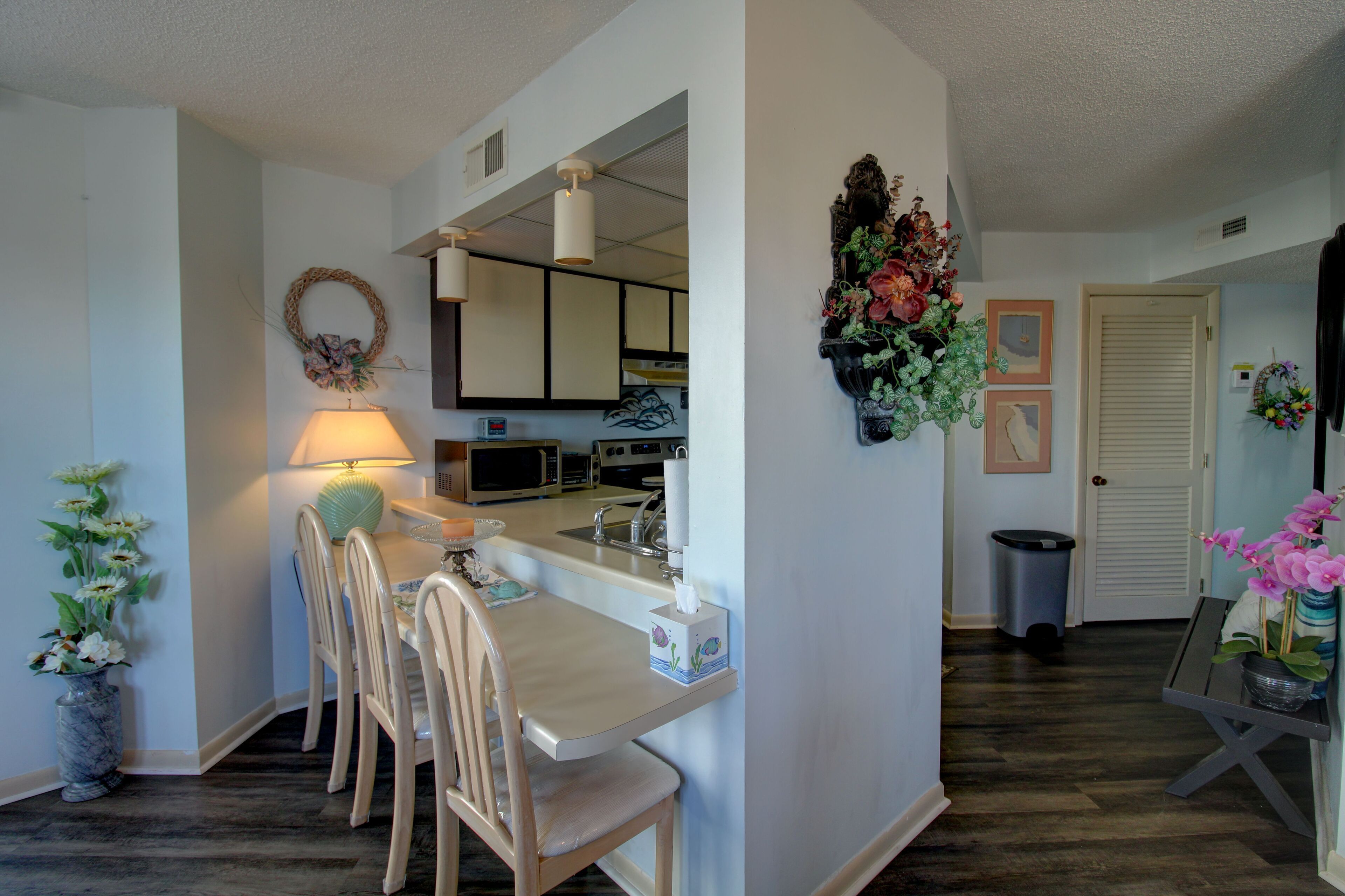 A dining area with a table, chairs, a lamp, and a vase of flowers.
