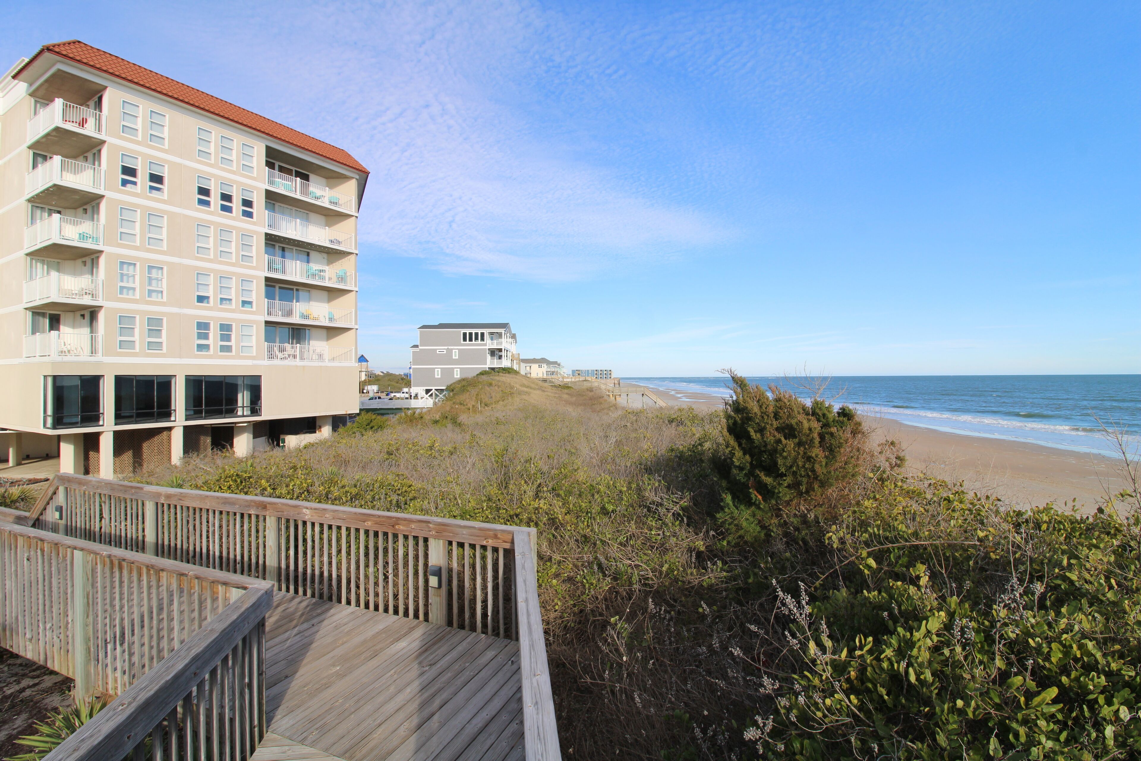 A beachfront hotel with multiple balconies, a wooden deck, and a view of the ocean.