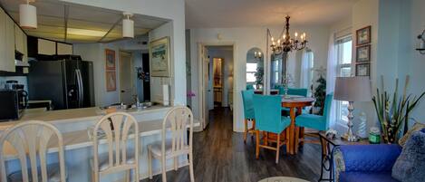 A modern kitchen with a refrigerator, dining area with chairs, and a living room with a sofa and a coffee table.