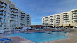 Une piscine entourée d’une terrasse en briques, avec des chaises longues et un petit pavillon.