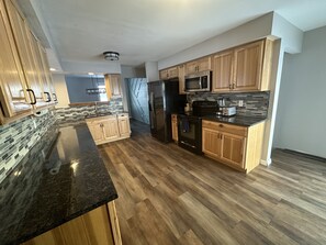 A modern kitchen with wooden cabinets, a black refrigerator, and a granite countertop.