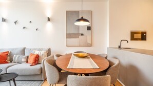 Ein modernes Wohnzimmer mit grauem Sofa, einem runden Esstisch aus Holz und einer Küchenzeile inklusive Einbau-Mikrowelle.