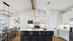 Una cocina moderna con armarios blancos, una isla central con taburetes y un amplio ventanal que proporciona luz natural.