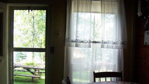 Una habitación con una mesa de comedor y sillas, una ventana con cortinas de encaje y vistas a una mesa de picnic en el exterior.