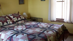 Un dormitorio con una cama grande, una mesita de noche, una lámpara y una ventana con cortinas.