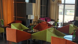 A modern hotel lobby with vibrant chairs, a central table, and large windows offering a view of the outside. - Hotel Al Shahba Jeddah   (Jeddah)