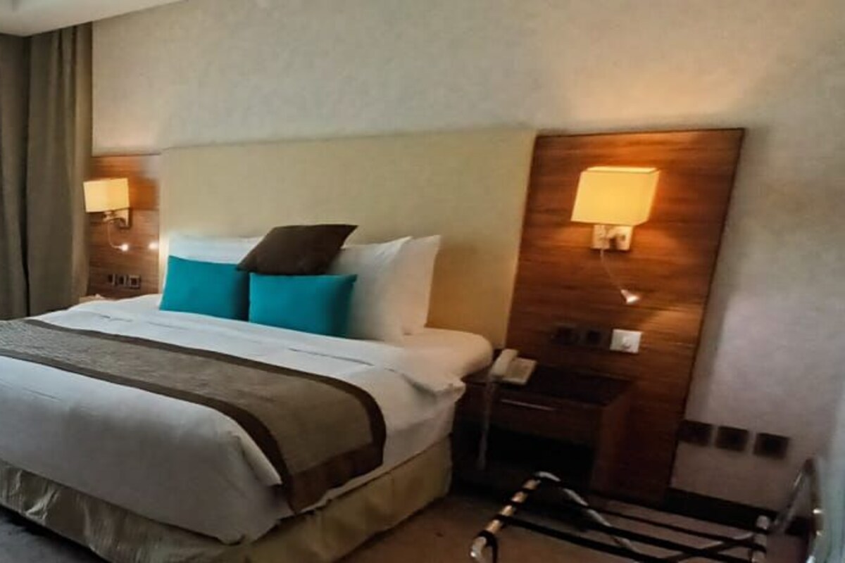 Une chambre d’hôtel avec un grand lit, une chaise, une petite table et une fenêtre avec des rideaux.