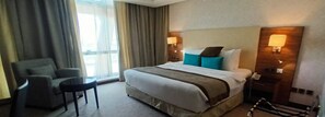 Une chambre d’hôtel avec un grand lit, une chaise, une petite table et une fenêtre avec des rideaux.