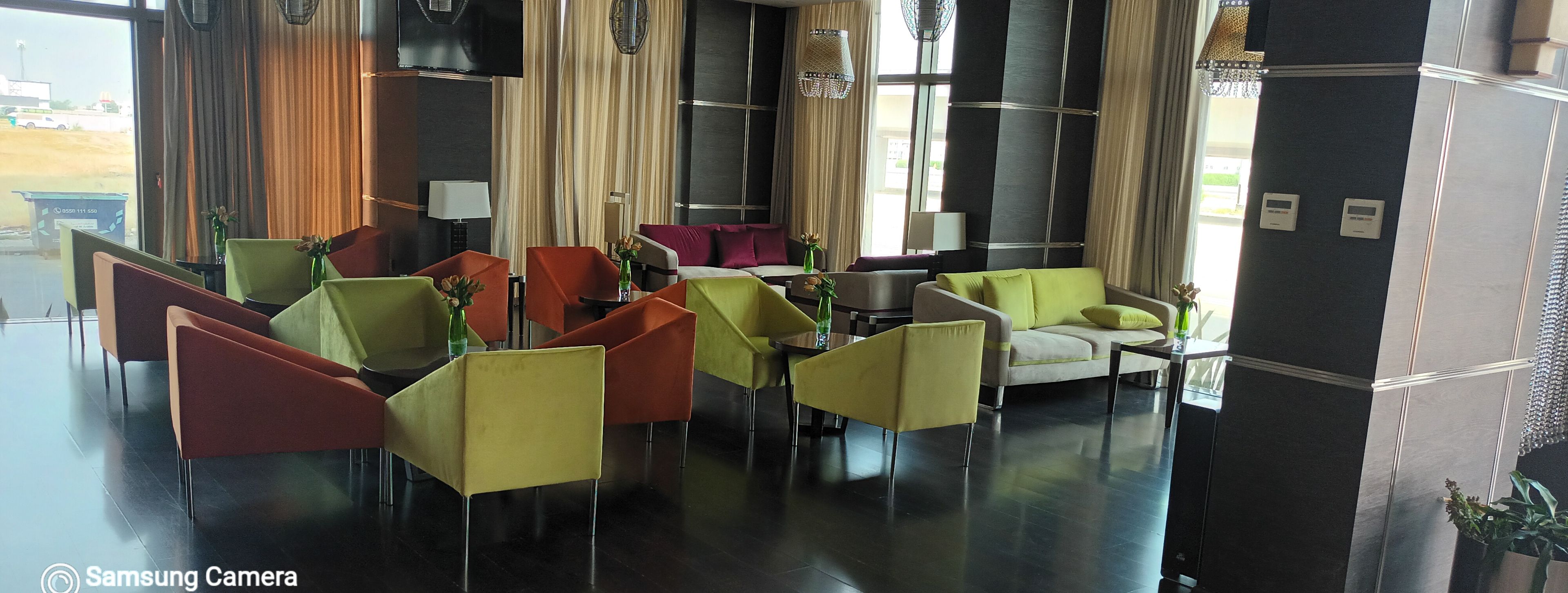 A hotel lobby with multiple seating areas, including chairs and sofas, and a large window providing a view of the outside.