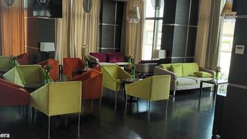 A hotel lobby with multiple seating areas, including chairs and sofas, and a large window providing a view of the outside.