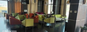 Un hall d’hôtel doté de plusieurs espaces aménagés avec des sièges, notamment des chaises et des canapés, et d’une grande fenêtre offrant une vue sur l’extérieur.