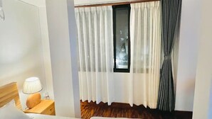 Une chambre d’hôtel avec un grand lit, une table de chevet avec une lampe, une fenêtre avec des rideaux et un plancher en bois.
