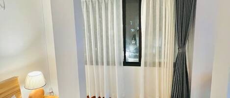 Una habitación de hotel con una cama grande, una mesita de noche con lámpara, una ventana con cortinas y suelo de madera.