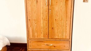 Une armoire en bois à deux portes et dotée d’un tiroir inférieur, un lit avec une couette blanche et un parquet en bois à motifs.