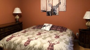 Une chambre à coucher comprenant un lit, deux lampes, une commode et trois tableaux représentant des cerfs, accrochés au mur.