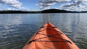 Un kayak sur une étendue d’eau calme, avec une rive bordée d’arbres et des collines en arrière-plan.