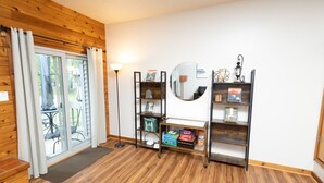 A room with wooden flooring, a sliding glass door leading to an outdoor area, a standing lamp, and two bookshelves with various items. - Family and pet-friendly, 2 Bedroom, 2 Bath, private townhome with wood-burning fireplace and jacuzzi tub (East Stroudsburg)