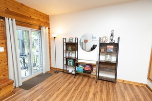A room with wooden flooring, a sliding glass door leading to an outdoor area, a standing lamp, and two bookshelves with various items. - Family and pet-friendly, 2 Bedroom, 2 Bath, private townhome with wood-burning fireplace and jacuzzi tub (East Stroudsburg)