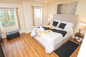 A bedroom with a bed, bedside lamps, a bench, and a view of the outdoors through windows. - Family and pet-friendly, 2 Bedroom, 2 Bath, private townhome with wood-burning fireplace and jacuzzi tub (East Stroudsburg)