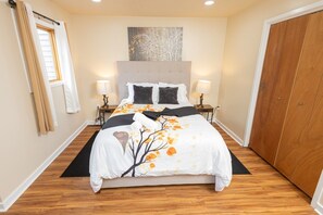 A hotel room with a large bed, two bedside tables with lamps, a window with curtains, a painting on the wall, and a wooden wardrobe.