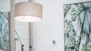 Ein Zimmer mit einer Hängelampe, einer Treppe und einem großen Gemälde einer tropischen Pflanze an der Wand.