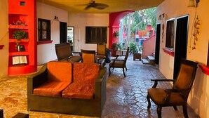 A cozy interior with a stone-tiled floor, a red accent wall, and a seating area with a sofa and chairs. - Hotel de Arnold (Mazatlán)
