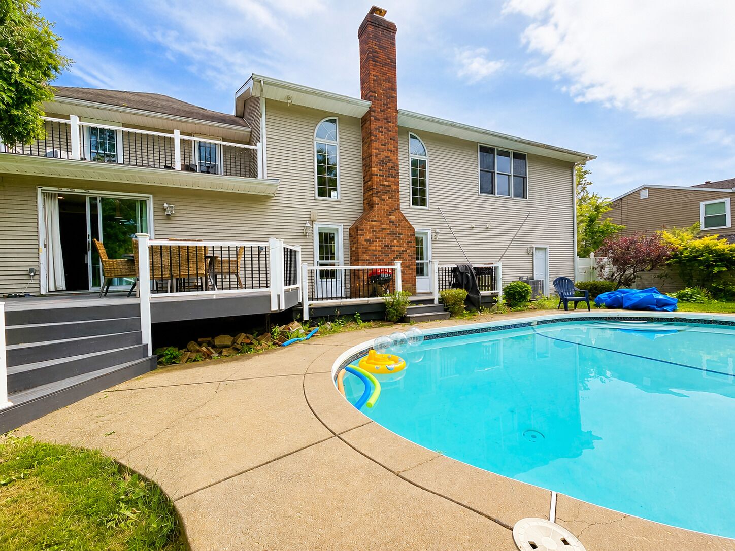 A two-story house with a swimming pool, a covered patio, and a brick chimney.