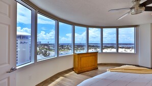 Un dormitorio con ventanas amplias, una mesita de noche de madera y una cama.