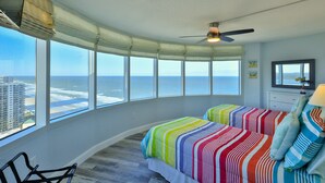 Ein Schlafzimmer mit gewölbter Decke, großen Fenstern, einem Bett mit farbenfroher Bettwäsche, einem Deckenventilator und Blick auf den Ozean.
