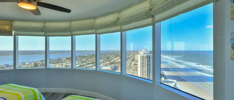 A room with a curved window overlooking a beach and cityscape.