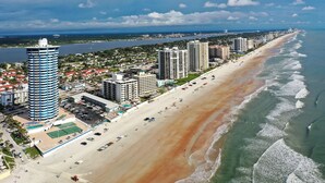 A coastal cityscape with a long sandy beach, high-rise buildings, and a clear view of the ocean. - SEASHELL SERENADE-24th Floor Ocean/River View - POOL, HOT TUB, Peck Plaza 2B/2B (Daytona Beach)