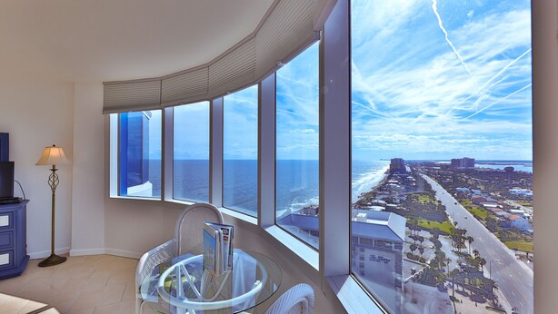 A high-rise room with a curved ceiling, large windows offering ocean views, a glass table, and a floor lamp. - SEASHELL SERENADE-24th Floor Ocean/River View - POOL, HOT TUB, Peck Plaza 2B/2B (Daytona Beach)