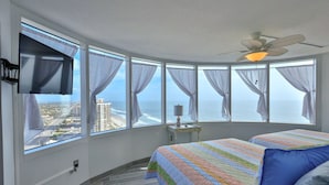 A bedroom with a large window, a bed, a ceiling fan, and a TV. - SAND CASTLE-Amazing Ocean Views,  Pool & HotTub PeckPlaza 23NW (Daytona Beach)