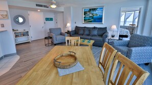 A living room with a wooden dining table, two patterned sofas, and a painting of a beach scene. - SAND CASTLE-Amazing Ocean Views,  Pool & HotTub PeckPlaza 23NW (Daytona Beach)
